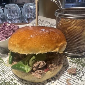 Burger s trhaným masem a salátem podávaný na novinovém papíře
